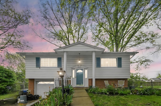 split foyer home featuring fence, an attached garage, and brick siding