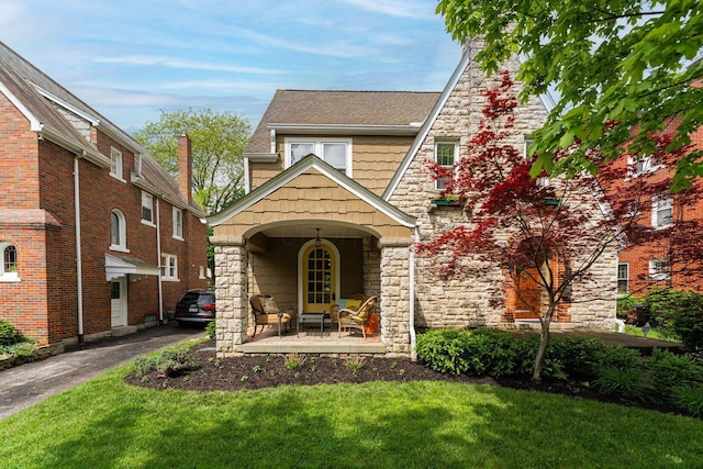 english style home featuring stone siding, a front lawn, and a porch