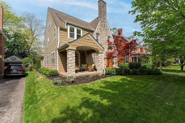 view of front of property with a porch, a front yard, stone siding, a chimney, and roof with shingles