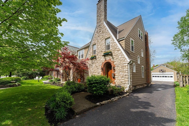 view of front facade with stone siding, an outdoor structure, a front lawn, a chimney, and a detached garage