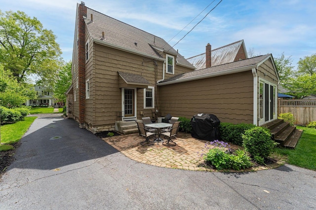 rear view of house featuring entry steps, roof with shingles, a patio area, and a chimney