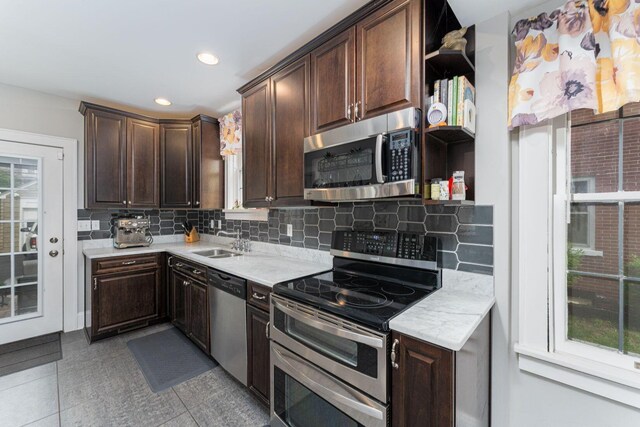 kitchen featuring appliances with stainless steel finishes, open shelves, a sink, dark brown cabinets, and decorative backsplash