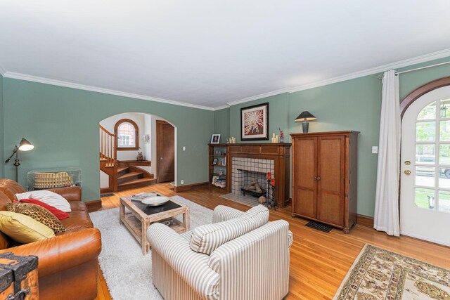 living room with arched walkways, stairs, crown molding, light wood finished floors, and a fireplace