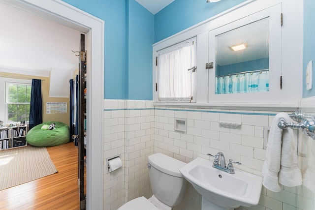 bathroom with a sink, toilet, tile walls, wainscoting, and wood finished floors