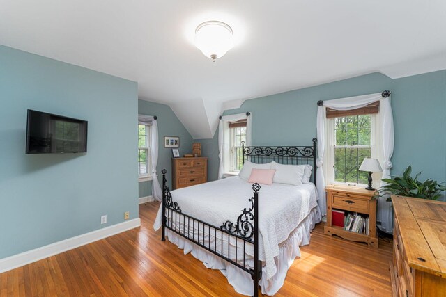 bedroom with wood finished floors, baseboards, and vaulted ceiling
