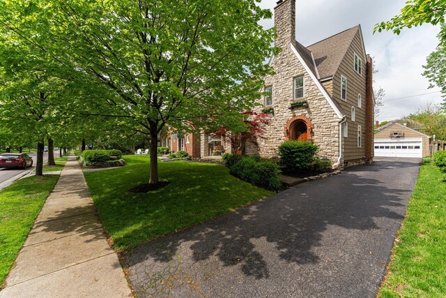 view of front of property featuring stone siding, a chimney, a front lawn, an outdoor structure, and a garage