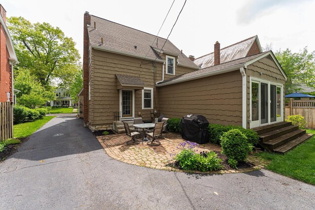back of house with entry steps, a chimney, a patio, and roof with shingles