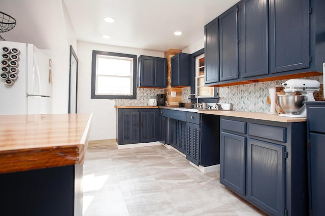 kitchen featuring freestanding refrigerator, tasteful backsplash, light countertops, a sink, and blue cabinetry