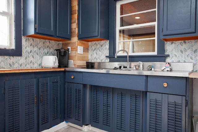 kitchen with blue cabinets, stainless steel countertops, tasteful backsplash, and a sink