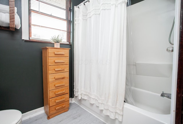 full bath featuring shower / bath combo, toilet, wood finished floors, and baseboards