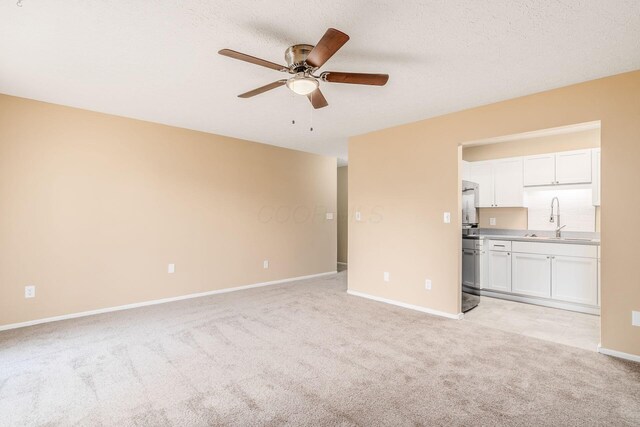 spare room featuring a sink, a ceiling fan, light colored carpet, and baseboards