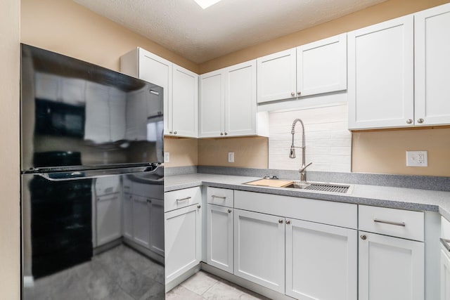 kitchen featuring freestanding refrigerator, a sink, white cabinets, light countertops, and a textured ceiling