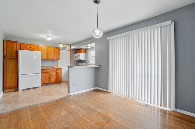 kitchen featuring white appliances, light countertops, light wood-style floors, and brown cabinets