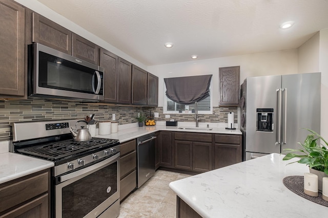 kitchen featuring appliances with stainless steel finishes, a sink, dark brown cabinetry, tasteful backsplash, and recessed lighting