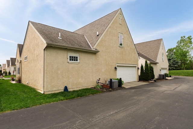 9785 Kingston Cir, Powell, OH 43065 - view of property exterior featuring roof with shingles, stucco siding, asphalt driveway, a lawn, and cooling unit