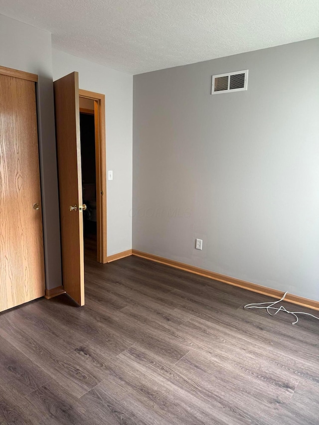 unfurnished bedroom with dark wood-style floors, baseboards, a closet, and a textured ceiling