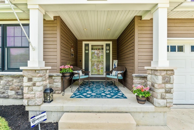 property entrance with a porch, stone siding, and a garage