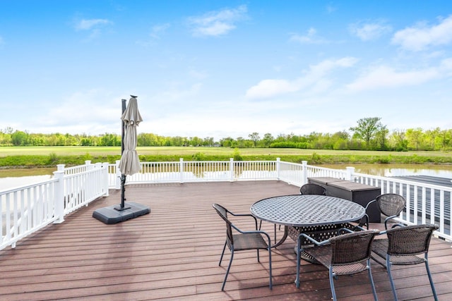wooden terrace featuring a water view, outdoor dining area, and view of scattered trees