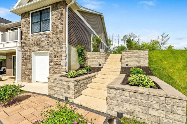 view of side of home featuring stone siding, a balcony, and stairs