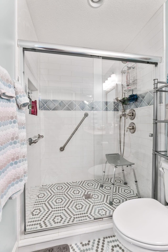 bathroom with toilet, a shower stall, tile patterned floors, and a textured ceiling