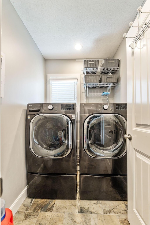 laundry area with washing machine and clothes dryer, baseboards, a textured ceiling, and stone finish floors
