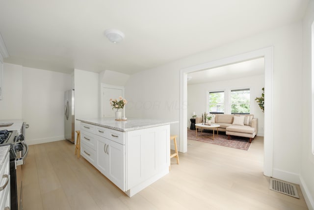 kitchen featuring stainless steel range with gas stovetop, light wood-style flooring, freestanding refrigerator, white cabinetry, and light stone counters