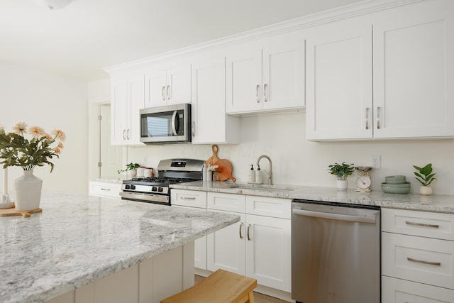 kitchen with stainless steel appliances, a sink, white cabinetry, and light stone counters