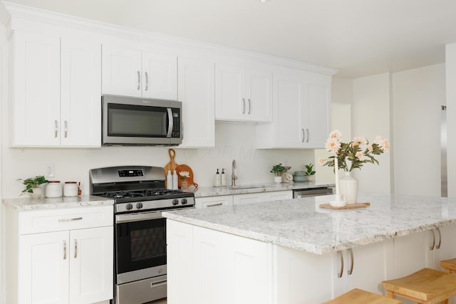 kitchen with stainless steel appliances, a sink, a kitchen island, white cabinetry, and a breakfast bar area