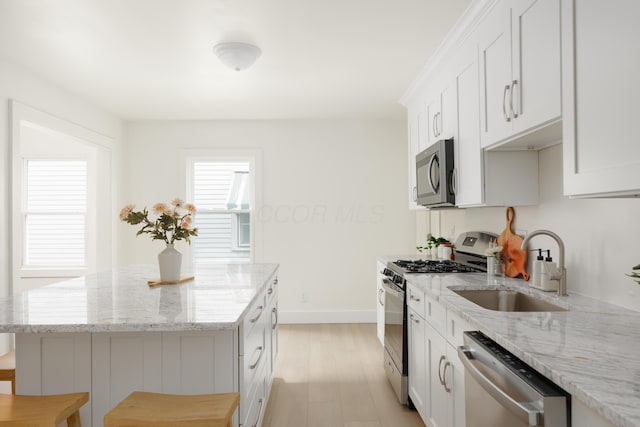 kitchen featuring appliances with stainless steel finishes, a sink, a kitchen island, light wood finished floors, and light stone countertops