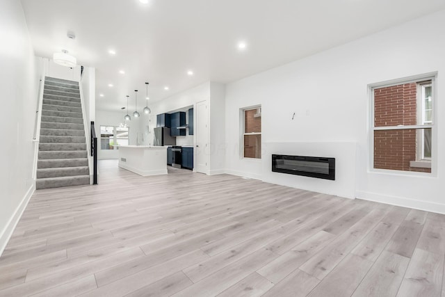 1177 Franklin Ave, Columbus, OH 43205 - unfurnished living room featuring light wood finished floors, heating unit, stairway, a glass covered fireplace, and baseboards