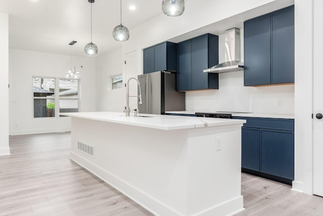 1177 Franklin Ave, Columbus, OH 43205 - kitchen featuring wall chimney exhaust hood, blue cabinets, freestanding refrigerator, light wood-type flooring, and a kitchen island with sink