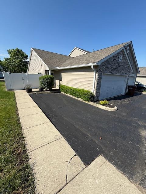 6983 Remsen Dr Unit 77A, Canal Winchester, OH 43110 - view of side of home with asphalt driveway, an attached garage, fence, and a shingled roof