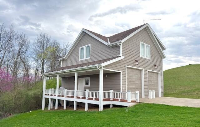 view of front of house with an attached garage, a porch, driveway, and a front yard