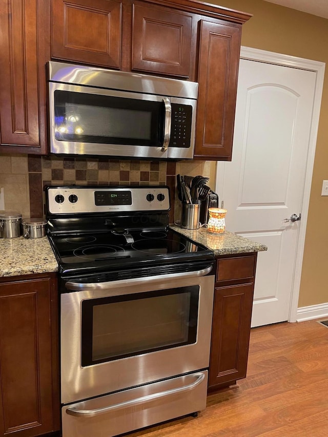 7719 Bear Run Rd, Logan, OH 43138 - kitchen with stainless steel appliances, light wood-type flooring, backsplash, light stone countertops, and baseboards