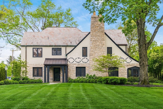 tudor home with stone siding, a front lawn, a standing seam roof, and stucco siding
