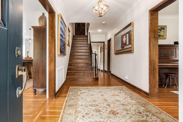 entryway with stairway, crown molding, light wood-style floors, baseboards, and a chandelier