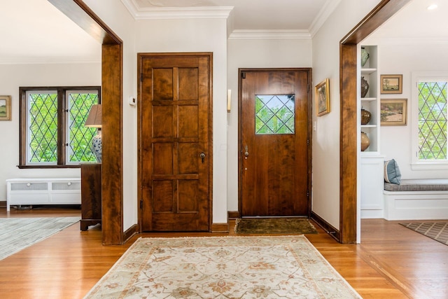 entrance foyer with radiator, wood finished floors, ornamental molding, and baseboards