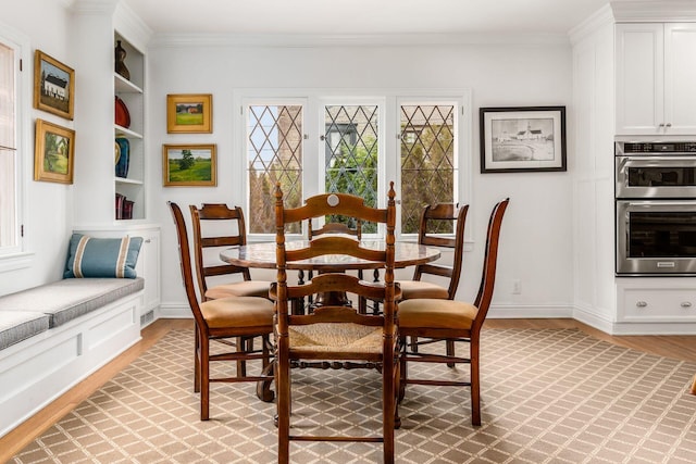dining area featuring light wood finished floors, ornamental molding, baseboards, and built in shelves