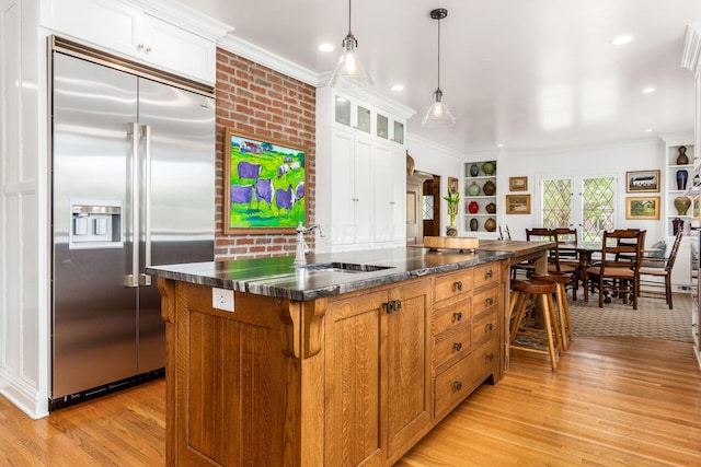 kitchen featuring built in fridge, dark countertops, light wood-type flooring, crown molding, and a sink
