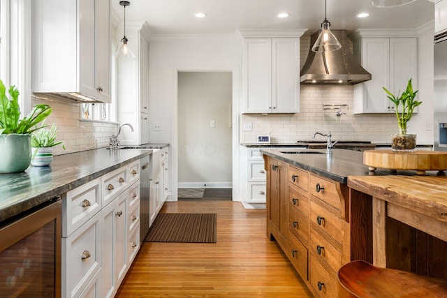kitchen featuring beverage cooler, wall chimney range hood, light wood finished floors, backsplash, and a sink
