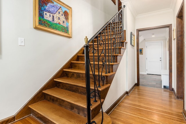 stairs with ornamental molding, wood finished floors, and baseboards