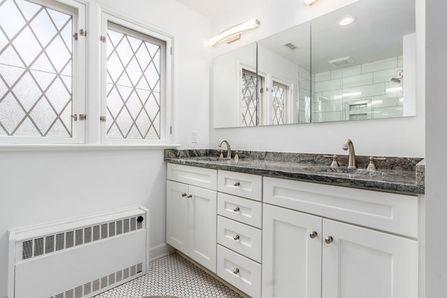 bathroom with radiator, double vanity, an enclosed shower, tile patterned floors, and baseboards