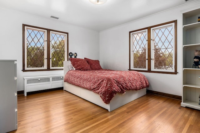 bedroom featuring wood finished floors, ornamental molding, baseboards, and multiple windows