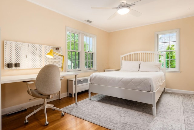 bedroom with radiator, crown molding, multiple windows, wood finished floors, and baseboards