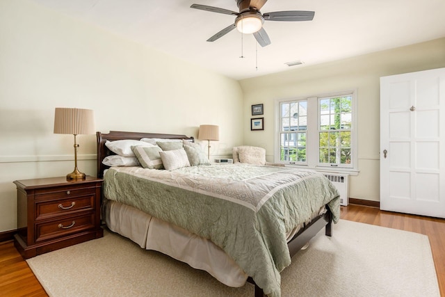 bedroom featuring radiator, wood finished floors, ceiling fan, and baseboards