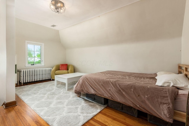 bedroom featuring radiator heating unit, wood finished floors, and vaulted ceiling