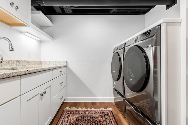 clothes washing area with washer and dryer, dark wood-type flooring, baseboards, and cabinet space