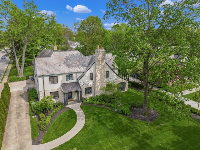 tudor home featuring a chimney, stucco siding, a front lawn, stone siding, and a standing seam roof