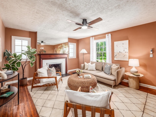 living room featuring a ceiling fan, baseboards, light wood-style floors, and a textured ceiling
