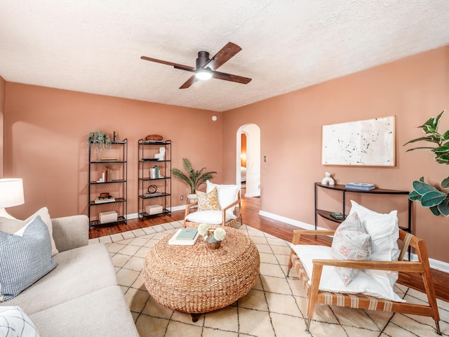 living room featuring arched walkways, a ceiling fan, baseboards, wood finished floors, and a textured ceiling
